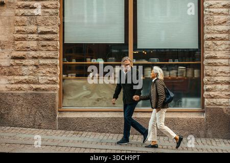 Seniorenpaar, das Hände hält, während er in der Nähe des Ladengeschäfts auf der Straße spaziert Stockfoto