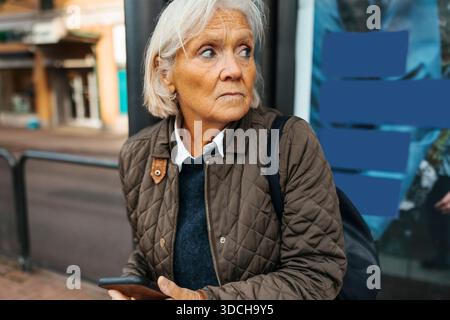 Weißhaarige ältere Frau, die wegschaut, während sie an der Bushaltestelle wartet Stockfoto