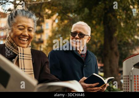 Senior-Mann, der ein Buch hält und mit einer Frau spricht, die auf der Straße Zeitung liest Stockfoto