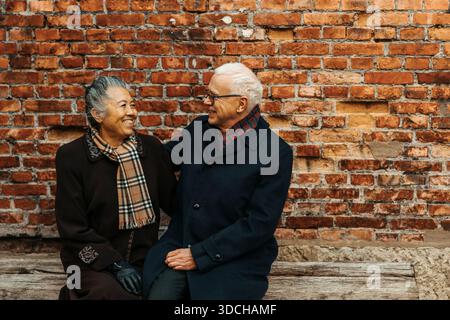 Glückliche Seniorin, die mit einem Mann in der Nähe einer Mauer sitzt Stockfoto