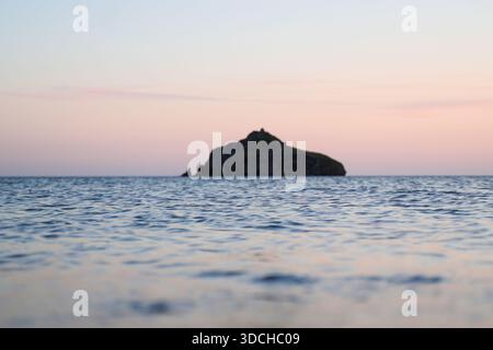 Kleine Insel, die aus ruhigem Meereswasser mit weichem Pastellhimmel in der Abenddämmerung hervorragt Stockfoto