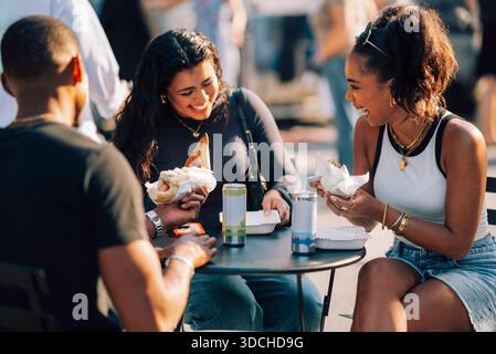 Glückliche Frau, die Fast Food mit Freunden genießt, während sie am Tisch sitzt Stockfoto