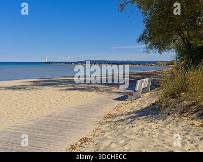 Parkbank entlang der Promenade am Sandstrand mit entfernter Lichtstation am Lake Huron Stockfoto