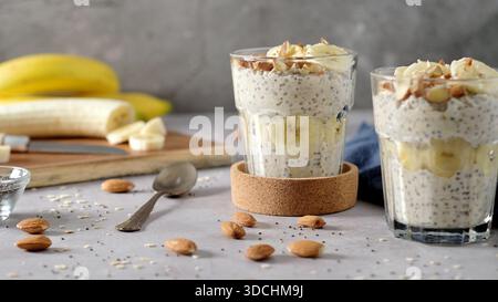 Zwei Gläser sind mit cremigem Chia-Samenpudding gefüllt, der mit frischen Bananenscheiben und knusprigen Mandeln belegt ist. Die helle, minimalistische Szene in Stockfoto