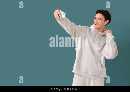Junger Mann im grauen Sportanzug, der Selfie auf blauem Hintergrund macht Stockfoto
