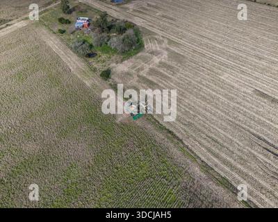 CANELONES, URUGUAY - 8. JULI 2024: Aus der Vogelperspektive eines Mähdreschers und eines Traktors, der auf einem Maisfeld neben einem ländlichen Bauernhaus und Garten in arbeitet Stockfoto