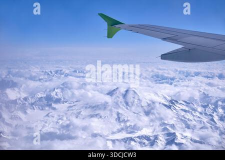 Der schneebedeckte Mount Elbrus mit seinem felsigen Gipfel, der in einer Winterlandschaft aus den Wolken ragt. Blick aus einem Flugzeug. Stockfoto
