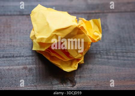 Ein eng zerknittertes Stück gelbes Papier, das auf eine dunkle Holzoberfläche mit sichtbaren Körnungen gelegt wird. Stockfoto