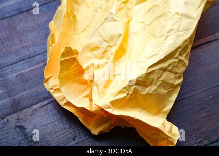 Ein stark zerknittertes gelbes Papier liegt auf einer dunklen Holzoberfläche, die eine satte Textur und einen satten Kontrast aufweist. Stockfoto