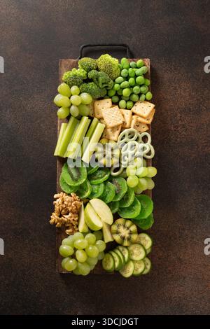 Grüne Snacktafel mit Obst, Gemüse und knusprigen Snacks, zubereitet für die St. Patrick's Day Feier auf hellem Hintergrund. Blick von oben. Stockfoto