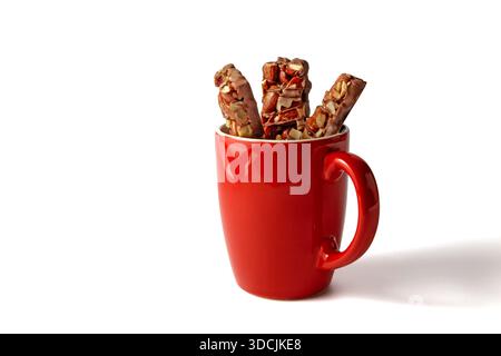 Karamell- und Nussriegel mit Schokoladenglasur in einer roten Kaffeetasse. Stockfoto