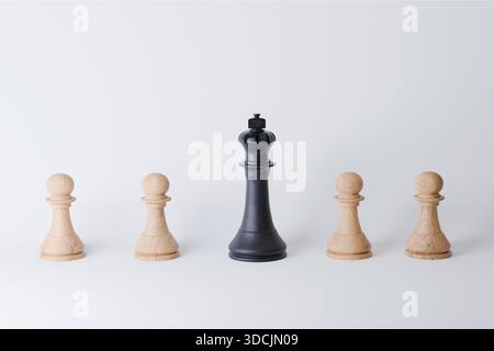 Hölzerne Schachfiguren und schwarzer Schachkönig auf weißem Hintergrund, Konzept. Strategie, Führung und Geschäft, kreative Idee. Denken Sie anders Stockfoto