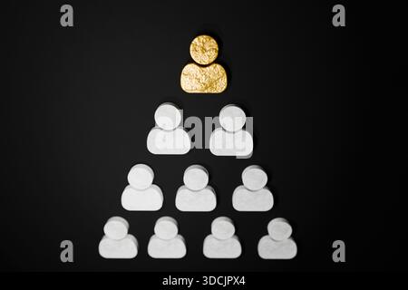 Goldene Figur an der Spitze einer menschlichen Pyramide auf schwarzem Hintergrund, symbolisiert Karriereentwicklung, Führung, Hierarchie, Personalmanagement, Mitarbeiterentwicklung Stockfoto