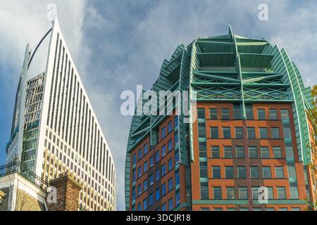 Blick auf moderne Architektur mit einem geometrischen weißen Gebäude und einem braunen Gebäude mit grünen Akzenten vor einem bewölkten Himmel, den Haag, South Hollan Stockfoto