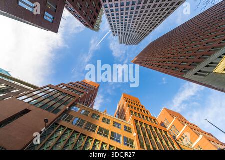 Blick auf rote und rosa Backsteinhäuser, die bis zu einem blauen Himmel mit verstreuten Wolken aus einer niedrigen Perspektive reichen, den Haag, Südholland, Niederlande Stockfoto