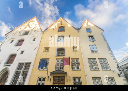 Blick auf historische Gebäude mit spitzen Dächern, die hoch vor einem blauen Himmel stehen und unter den Fenstern hängen Fahnen in Tallinn, Harju County, Estland. Stockfoto