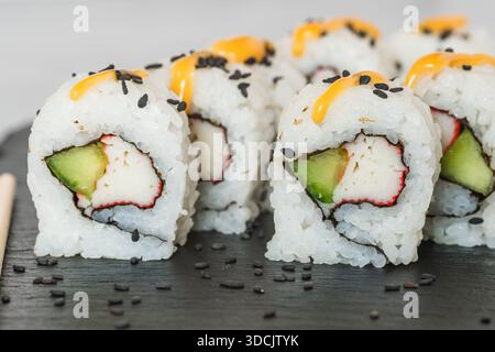 Nahaufnahme von kalifornischen Sushi-Brötchen, gefüllt mit nachgeahmten Krabben, Gurken, und garniert mit Sesamsamen und Soße. Stockfoto