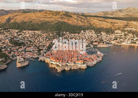 Blick aus der Vogelperspektive auf die Terrakotta-Dächer, die hinunterragen, um auf die azurblaue Adria zu treffen, die die alten Mauern von Dubrovnik, Kroatien, umschließt. Stockfoto