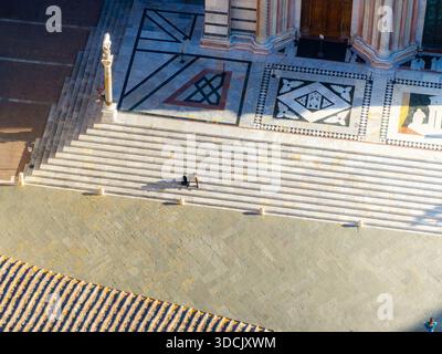 Aus der Vogelperspektive auf die Stufen, die zum Duomo di Siena führen, getaucht in warmes Sonnenlicht im Kontrast zu den kühlen Schatten der Marmormuster, Siena, Tu Stockfoto