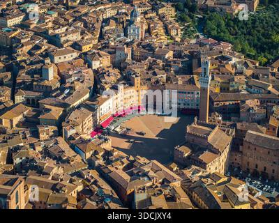 Aus der Vogelperspektive auf die sonnenverwöhnte Piazza del Campo und den Torre del Mangia, die lange Schatten über die alten Dächer werfen, Siena, Toskana, Italien. Stockfoto