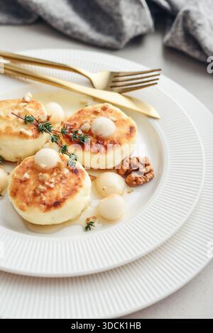 Weiße Platte mit Hüttenkäsepfannkuchen, Syrniki, Quark-Krapfen serviert mit Birnenbällchen, Walnuss und Honig auf hellem Hintergrund, Blick von oben Stockfoto