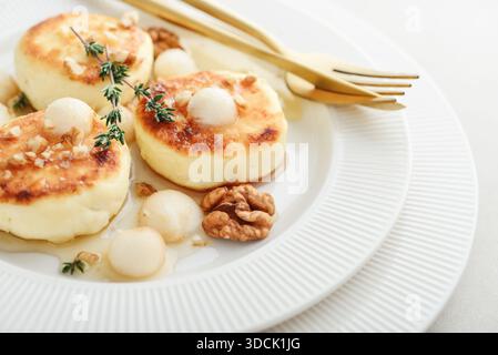 Weiße Platte mit Hüttenkäsepfannkuchen, Syrniki, Quark-Krapfen serviert mit Birnenbällchen, Walnuss und Honig auf hellem Hintergrund, Blick von oben Stockfoto