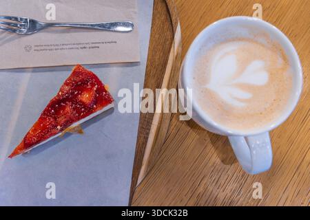 Horizontale Weitwinkelaufnahme von oben mit einem Stück Erdbeerkuchen und einer Tasse Kaffee auf einem Holztisch in einem Café, perfekt für Food-Blogging Stockfoto