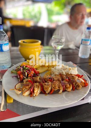 Gegrillte Hähnchenspieße, serviert mit Reisfritten und frischem Salat auf einem Café-Tisch. Zwangloses Essen, Essen im Freien, Reisevergnügen und jeden Tag Stockfoto