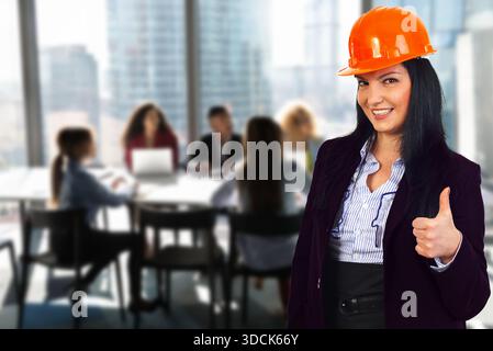 Eine Frau, die einen orangefarbenen Schutzhelm trägt, gibt einer Gruppe von Menschen den Daumen hoch. Konzept von Teamarbeit und Zusammenarbeit, während die Frau vor der Tür steht Stockfoto