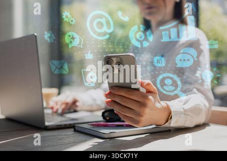 Geschäftsfrau mit Smartphone und Laptop am Schreibtisch, umgeben von digitalen Marketing- und KI-Symbolen. Konzept der modernen Technologie, Kommunikation, Daten ana Stockfoto