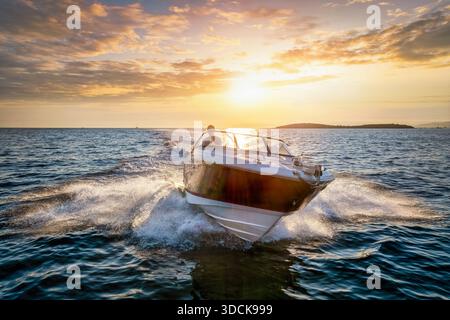 Aus der Vogelperspektive eines Sportmotorbootes, das während des Sonnenuntergangs im Sommer mit hoher Geschwindigkeit über das blaue Meer fährt Stockfoto
