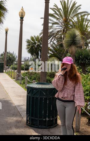 Frau mit rosafarbener MAGA-Mütze singt im palmengesäumten Park in Santa Monica, Kalifornien, USA Stockfoto