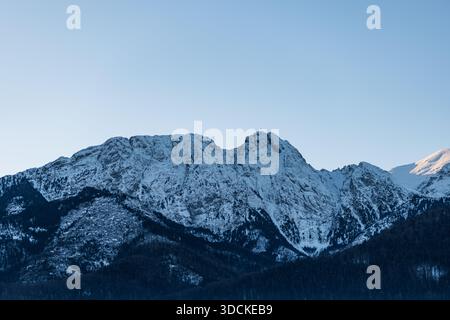 Atemberaubende Winterberglandschaft mit sonnendurchfluteten schneebedeckten Gipfeln im Kontrast zu den dunklen, bewaldeten Ausläufern. Leeren Sie den Kopierraum für Himmel Stockfoto