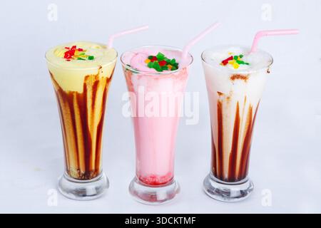 Drei bunte Eiscreme-Milchshakes, serviert in hohen Gläsern mit Strohhalmen, isoliert auf weißem Hintergrund. Stockfoto