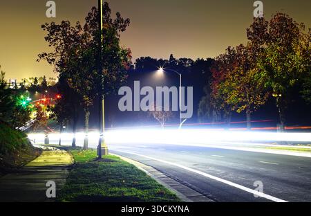 Helle, lange belichtete Lichtspuren auf einer ruhigen Vorstadtstraße bei Nacht Stockfoto