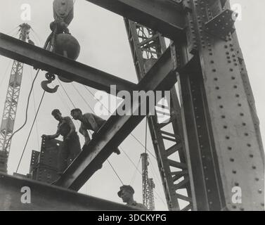 Bau des Empire State Building mit Stahlträgern und Eisenarbeitern bei der Arbeit in New York City, fotografiert von Lewis Wickes Hine, 1930–1931. - Dieses ikonische Foto von Lewis Wickes Hine dokumentiert den Bau des Empire State Building in den ersten Jahren der Großen Depression. Hine wurde beauftragt, das Projekt aufzunehmen und konzentrierte sich auf die Tapferkeit und das Können der Arbeiter – viele von ihnen eingewanderte Eisenarbeiter – auf freiliegenden Stahlträgern hoch über Manhattan. Das Bild symbolisiert die amerikanische industrielle Macht, Modernität und Optimismus sowie die menschliche Arbeit hinter einem der Stockfoto