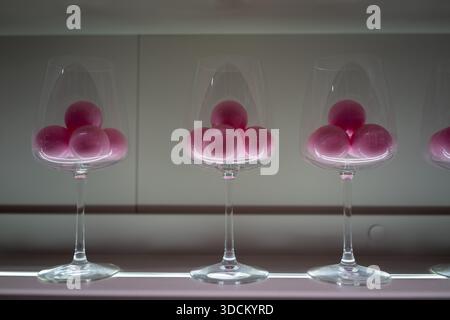 Reihe von Weingläsern gefüllt mit rosafarbenen Kugeln, symmetrisch angeordnet in einem minimalistischen Stillleben mit weichem Licht und sauberem Hintergrund. Stockfoto