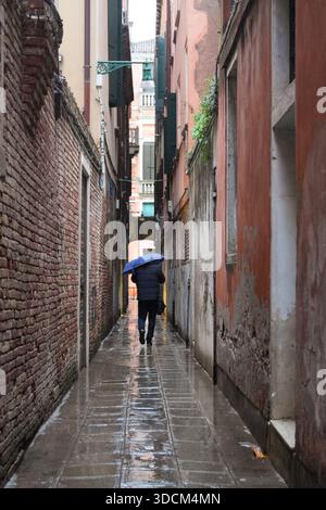 Reisen Sie italien venedig Person mit einem Regenschirm, der eine nasse, historische venezianische Gasse hinuntergeht Stockfoto
