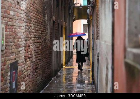 Reisen Sie italien venedig Person, die unter einem Sonnenschirm in einer engen, nassen Gasse mit historischen Backsteinmauern davonläuft Stockfoto