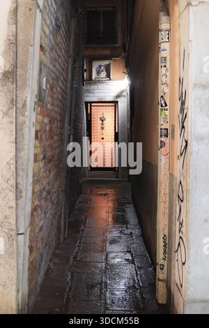 Reise italien venedig Dunkle, nasse calle in venedig reflektiert Umgebungslicht von einer entfernten Tür Stockfoto