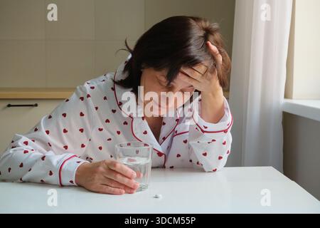 Frauen, die sich aufgrund von Kopfschmerzen unwohl fühlen Schmerzen, die Arzneimittel mit einem Glas Wasser einnehmen Stockfoto