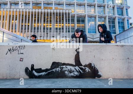 London, Großbritannien. Dezember 2025. Weihnachtseinkäufer und Touristen halten an, um herauszufinden, was ein neues Banksy-Kunstwerk sein könnte, das auf einer Betonbarriere vor dem Centrepoint an der Tottenham Court Road Station aufgetaucht ist. Es ist identisch mit einem anderen in West-London. Guy Bell/Alamy Live News Stockfoto