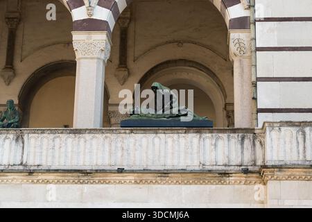Ausdrucksstarke Bronze-Grabskulptur einer trauernden getarnten Figur, die sich über den liegenden Körper auf dem Balkon der Arkade des Monumental-Friedhofs in Mailand beugt. Stockfoto