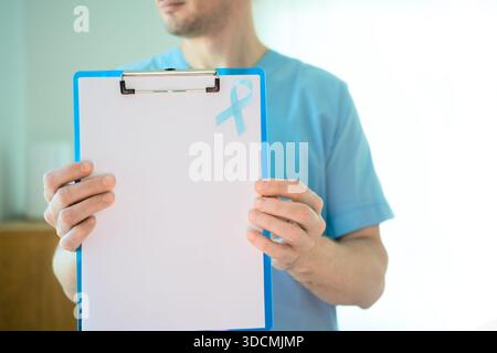 Mediziner-Mann in Uniform mit leerem Dokument mit blauem Band. Prostatakrebs-Bewusstseinssymbol im November, Früherkennung, Prävention und medizinisches Unterstützungskonzept. Stockfoto