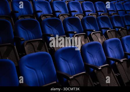 Reihen mit leeren blauen Stühlen bieten Sitzgelegenheiten in einem modernen Auditorium, Kino oder Konferenzsaal mit dunklen Akzenten Stockfoto