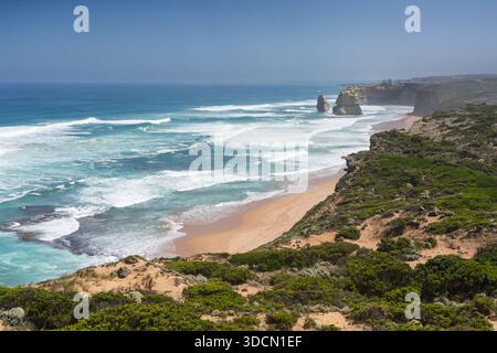 Ein erhöhter, weiter Blick entlang der zerklüfteten Küstenklippen, zeigt das tiefblaue und türkisfarbene Meer mit weißen Wellen, die auf einen Sandstrand brechen, und Stockfoto