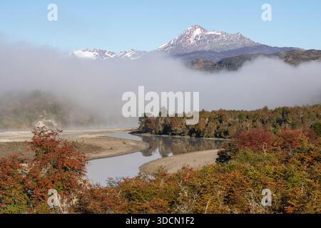 Ein breiter Blick auf ein Flusstal mit einer Kurve im Fluss, die den hellen Himmel reflektiert, umgeben von dickem Morgennebel, mit bunten Herbstbäumen und Stockfoto