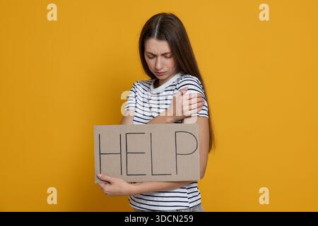 Besorgte Frau, die ein Schild mit Worthilfe auf gelbem Hintergrund hält Stockfoto