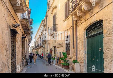 Die Menschen laufen auf der Via Principi Di Savoia, einer schmalen Straße im Zentrum des historischen Zentrums von Lecce in Italien, mit alten und mittelalterlichen Gebäuden. Stockfoto