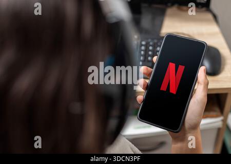 Ein nicht erkennbarer weiblicher Teenager hält ein Mobiltelefon mit einem Netflix-Logo auf dem Bildschirm mit schwarzem Hintergrund Stockfoto